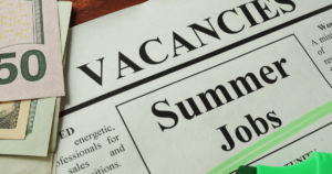 Image of a newspaper that reads "Vacancies. Summer Jobs" with summer jobs highlighted in green. Folded dollar bills are in the top left corner.