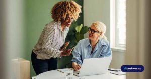 two woman collaborating over laptop in green office room